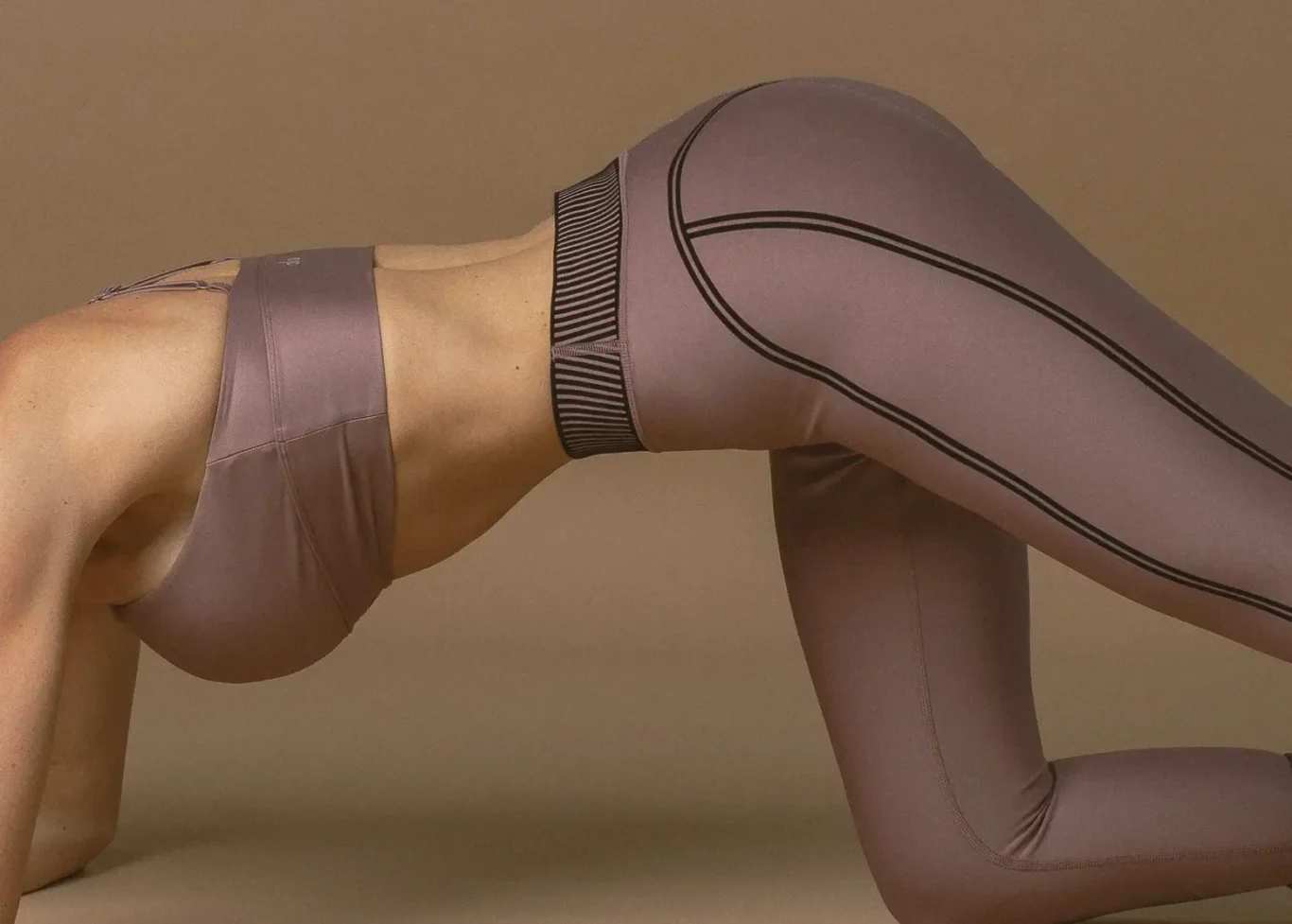 Person wearing lavender workout outfit on all fours, in a backbend stretch against a neutral background.