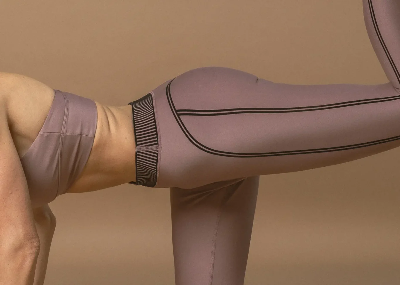 Person wearing lavender athletic leggings performing a leg stretch, with dark side stripes running along the leg.