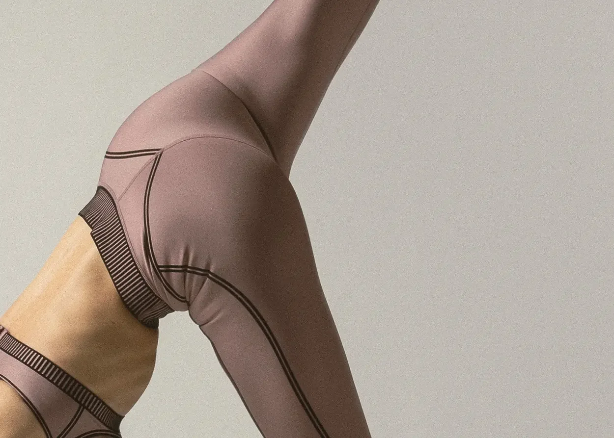 Close-up of a person in mauve athletic leggings raising one leg, highlighting the hip and thigh.
