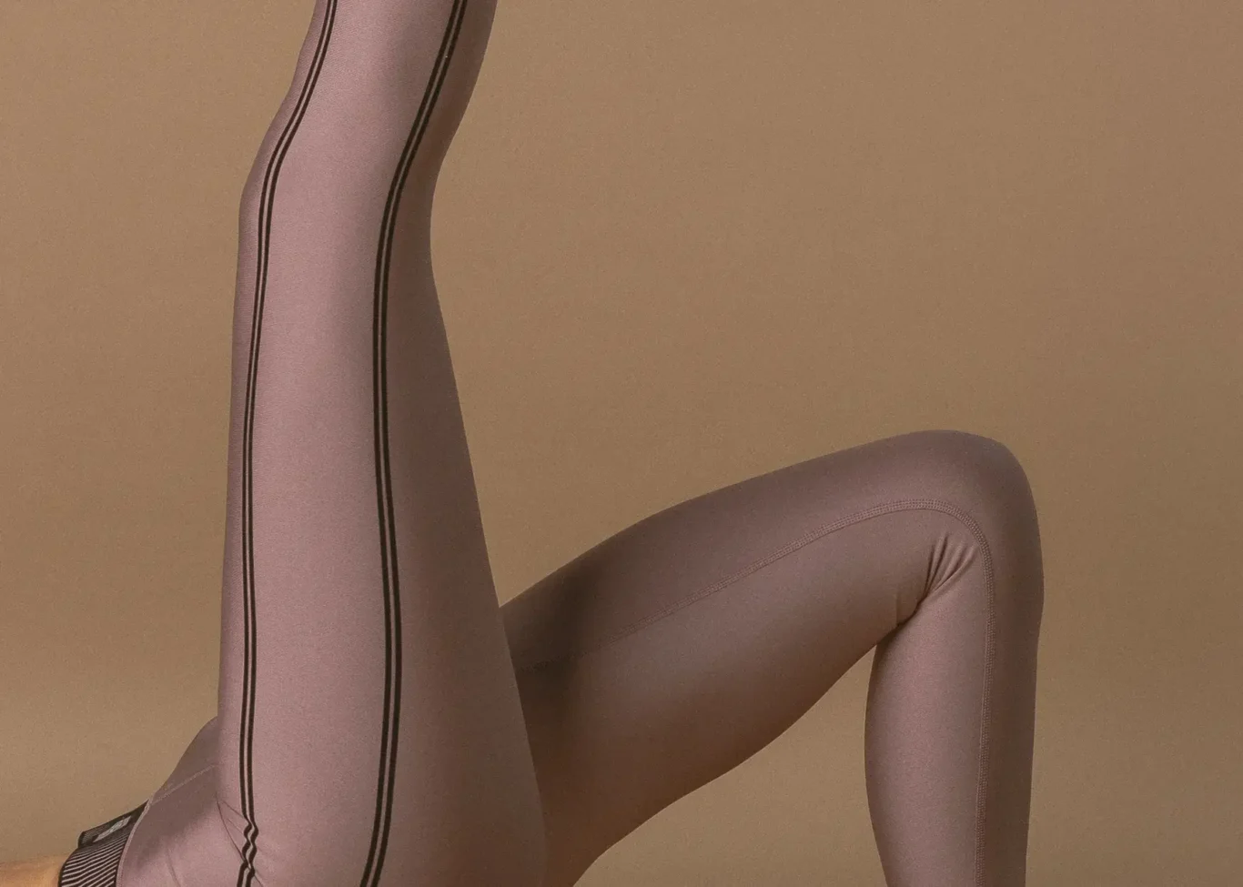Close-up of two legs in lavender tights with black side seams, one leg raised against a beige background.