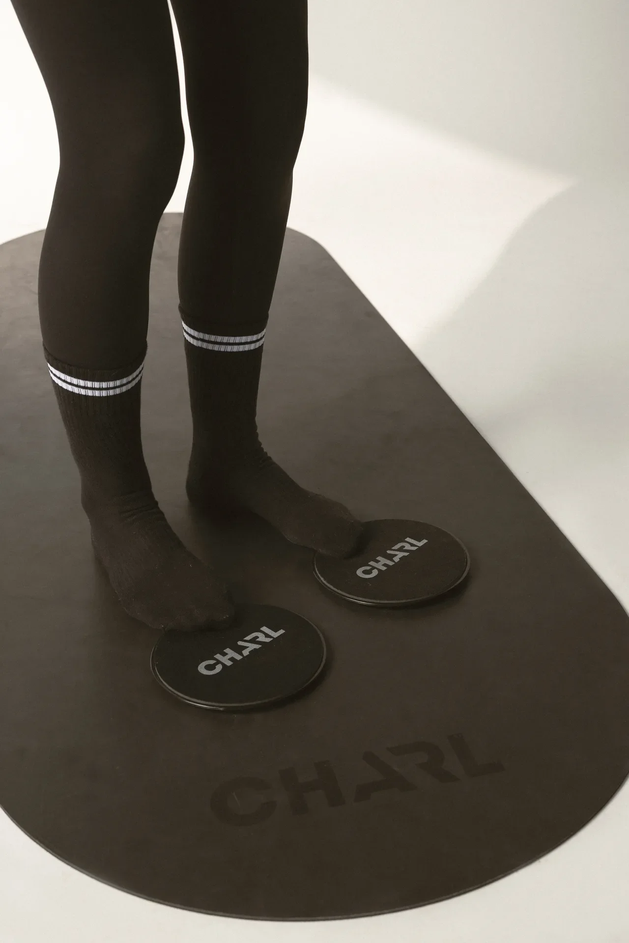 Person standing on a black exercise mat using two circular balance discs labeled CHARL.