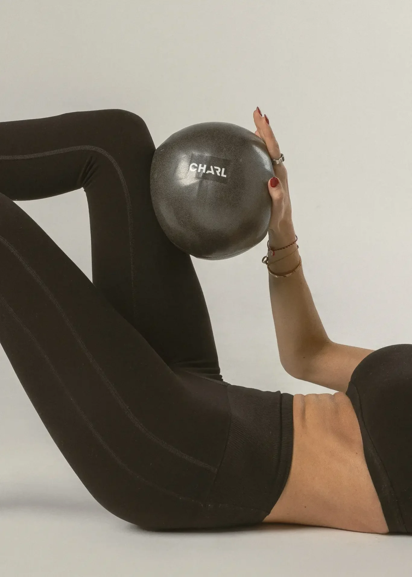 Person in black athletic leggings holding a gray exercise ball labeled 'CHARL' during a core exercise.
