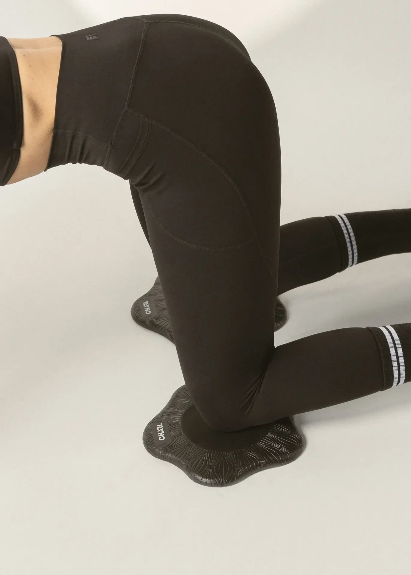Person in black athletic leggings kneeling in a yoga pose on textured balance discs used for stability training