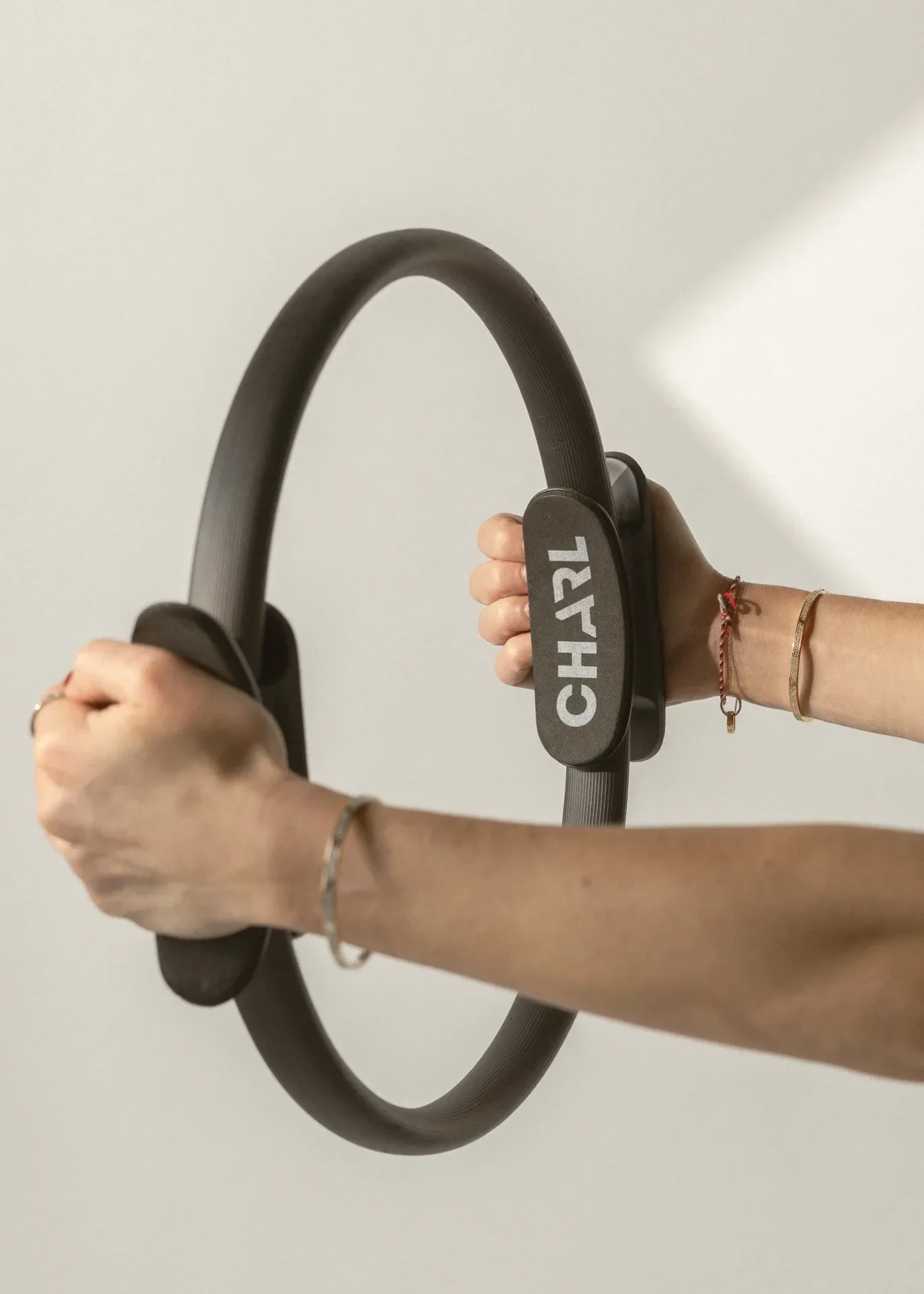 Close-up of a person gripping a large gray circular exercise ring with textured handles against a light background.