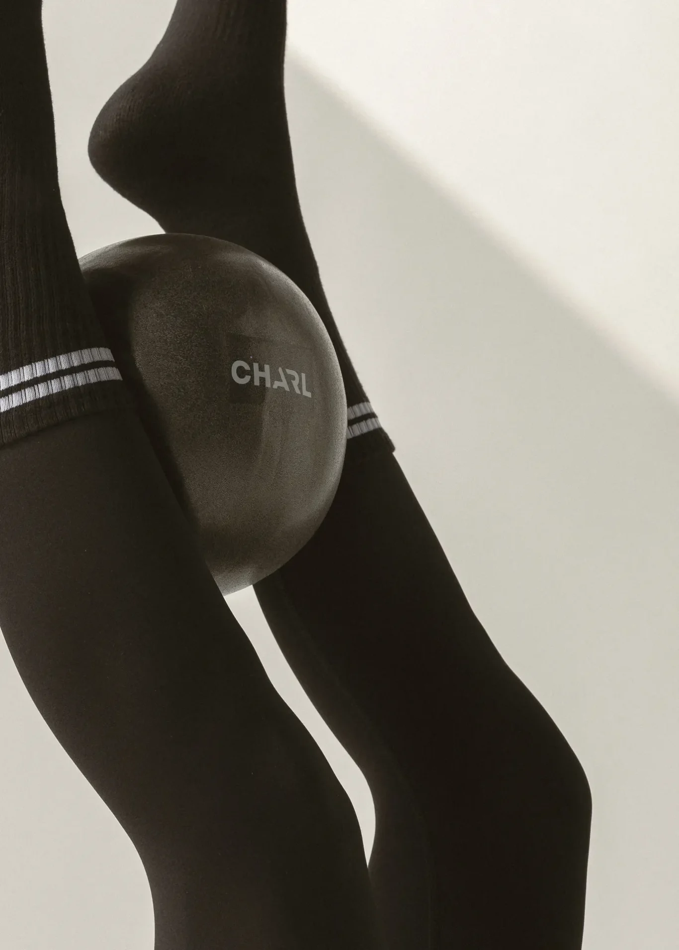 Close-up of black tights on legs with a large circular pad resting on the knee, the pad showing the word 'CHARL'.