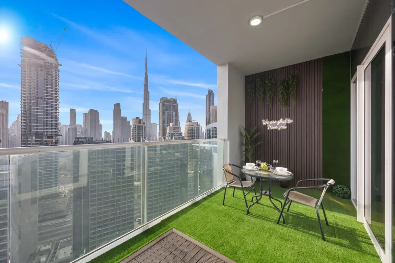 Balcony seating area with a round table set for two, overlooking a city skyline with tall skyscrapers and clear blue sky.