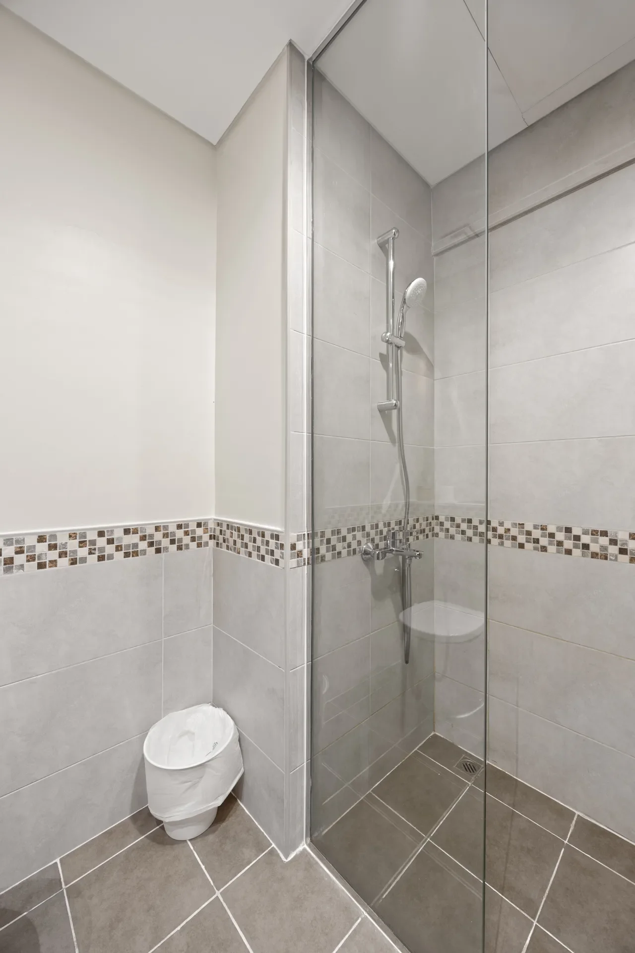 Modern bathroom shower with glass partition, wall-mounted handheld shower, and gray tile walls.