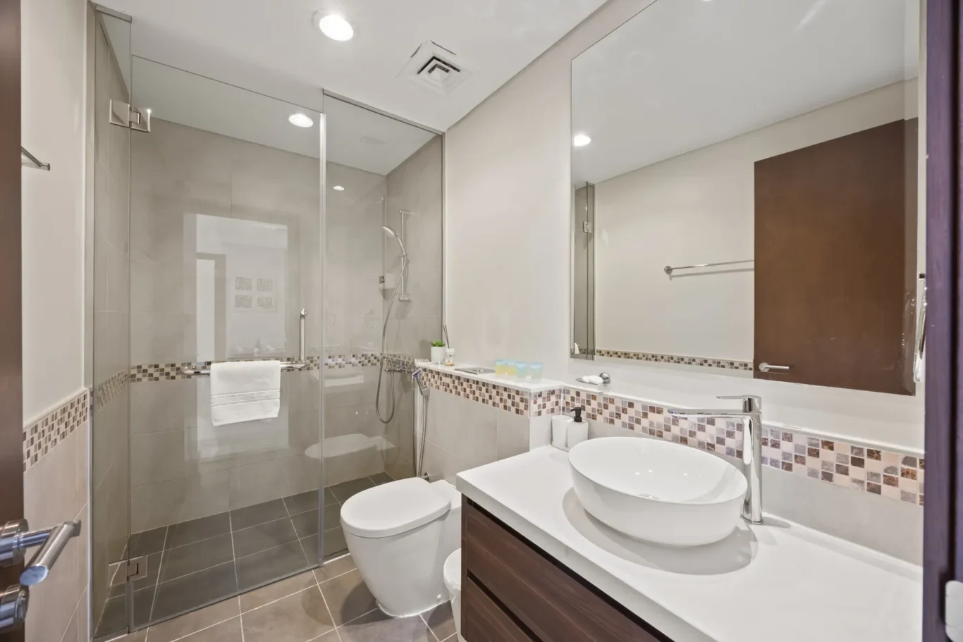 Modern bathroom with glass shower enclosure, wall-mounted vanity with round sink, and a tiled backsplash on the counter edge.