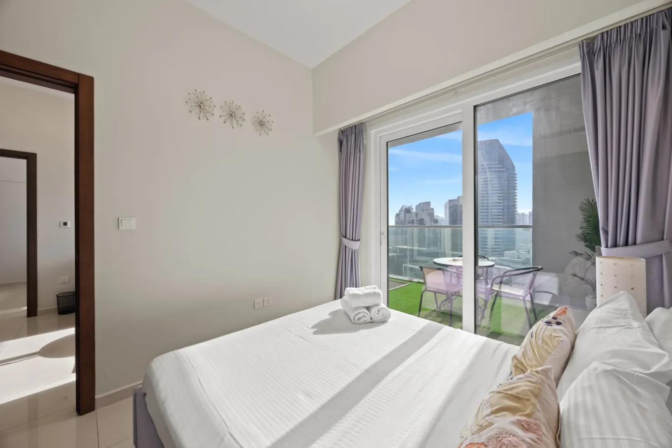 Twin beds with white linens and rolled towels, facing a balcony door with city skyline view