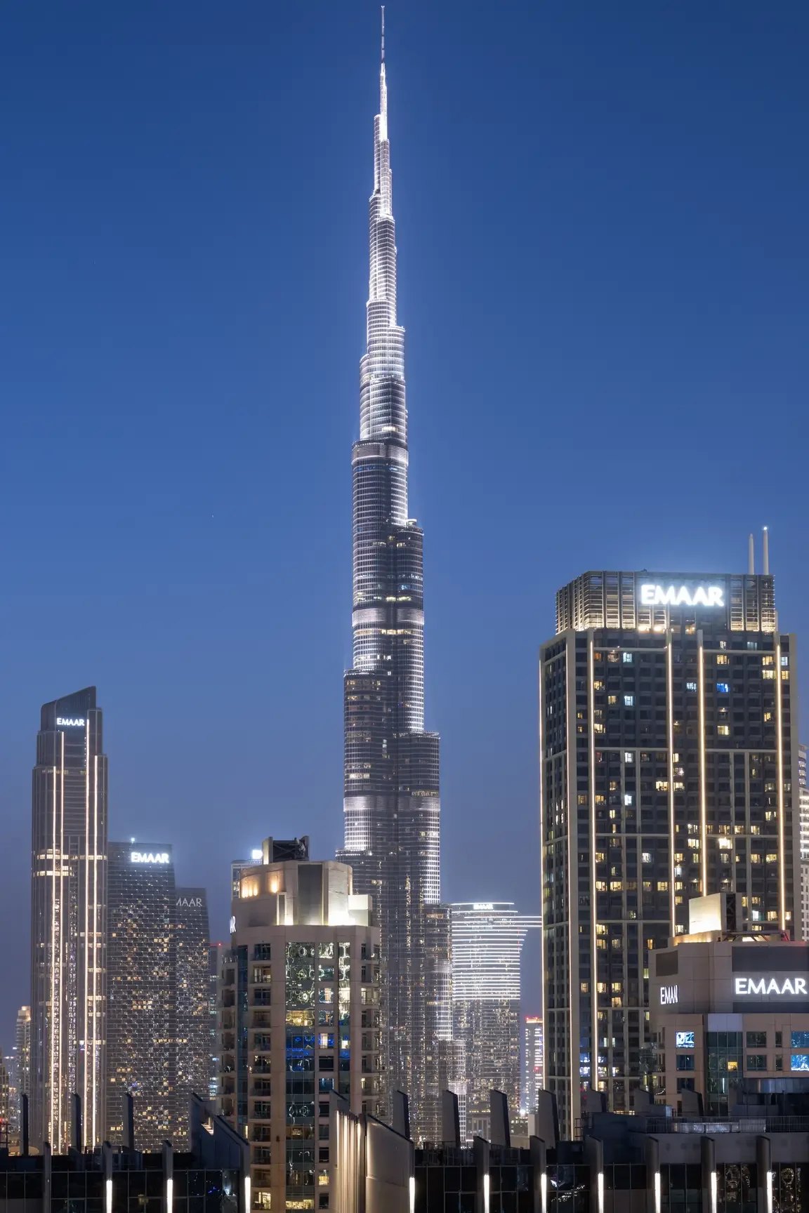 Burj Khalifa towering above Dubai skyline at dusk, surrounded by illuminated skyscrapers.