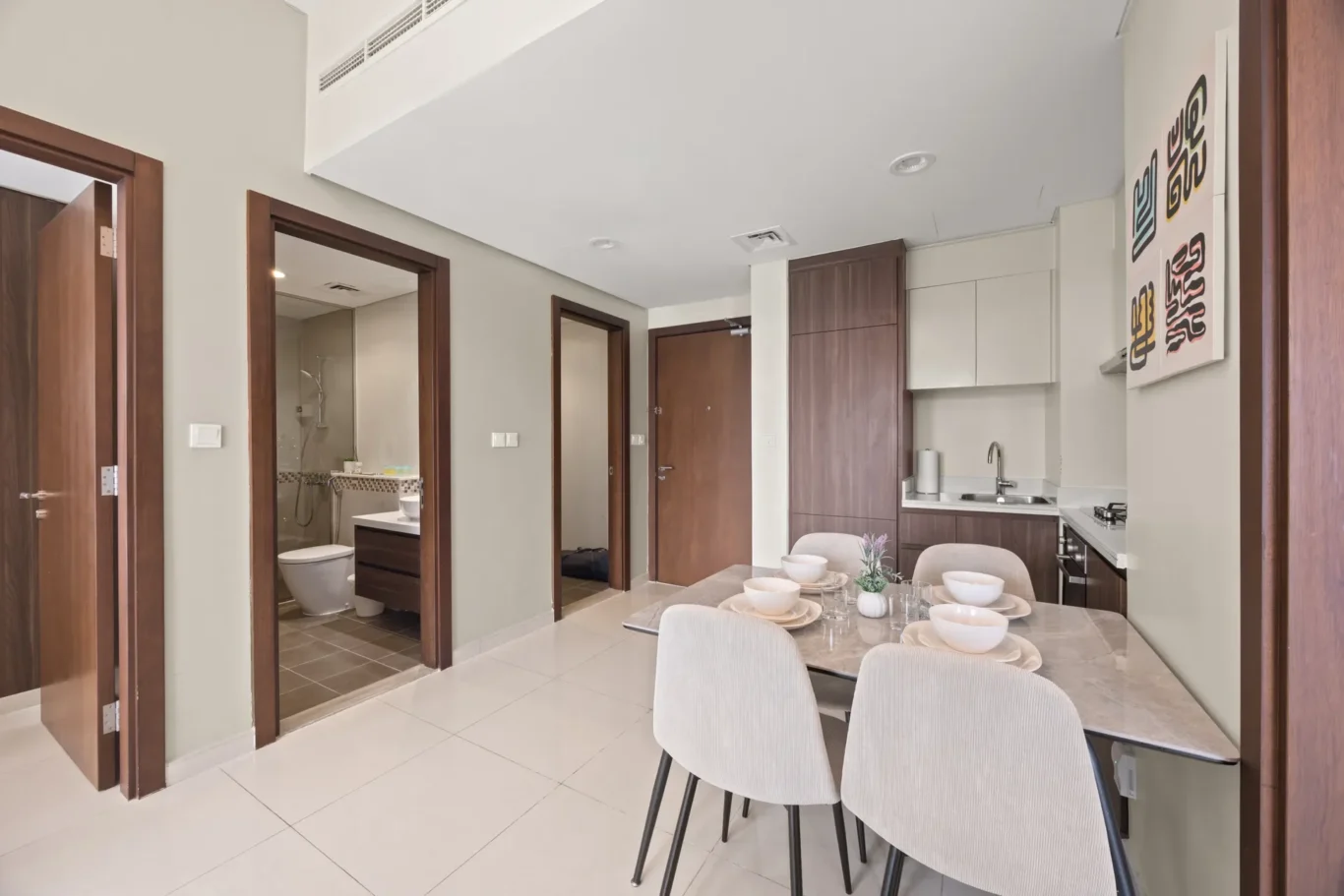 Open-concept dining area with a marble table set for six and beige chairs, adjacent to a modern kitchen with dark wood cabinets and white countertops.
