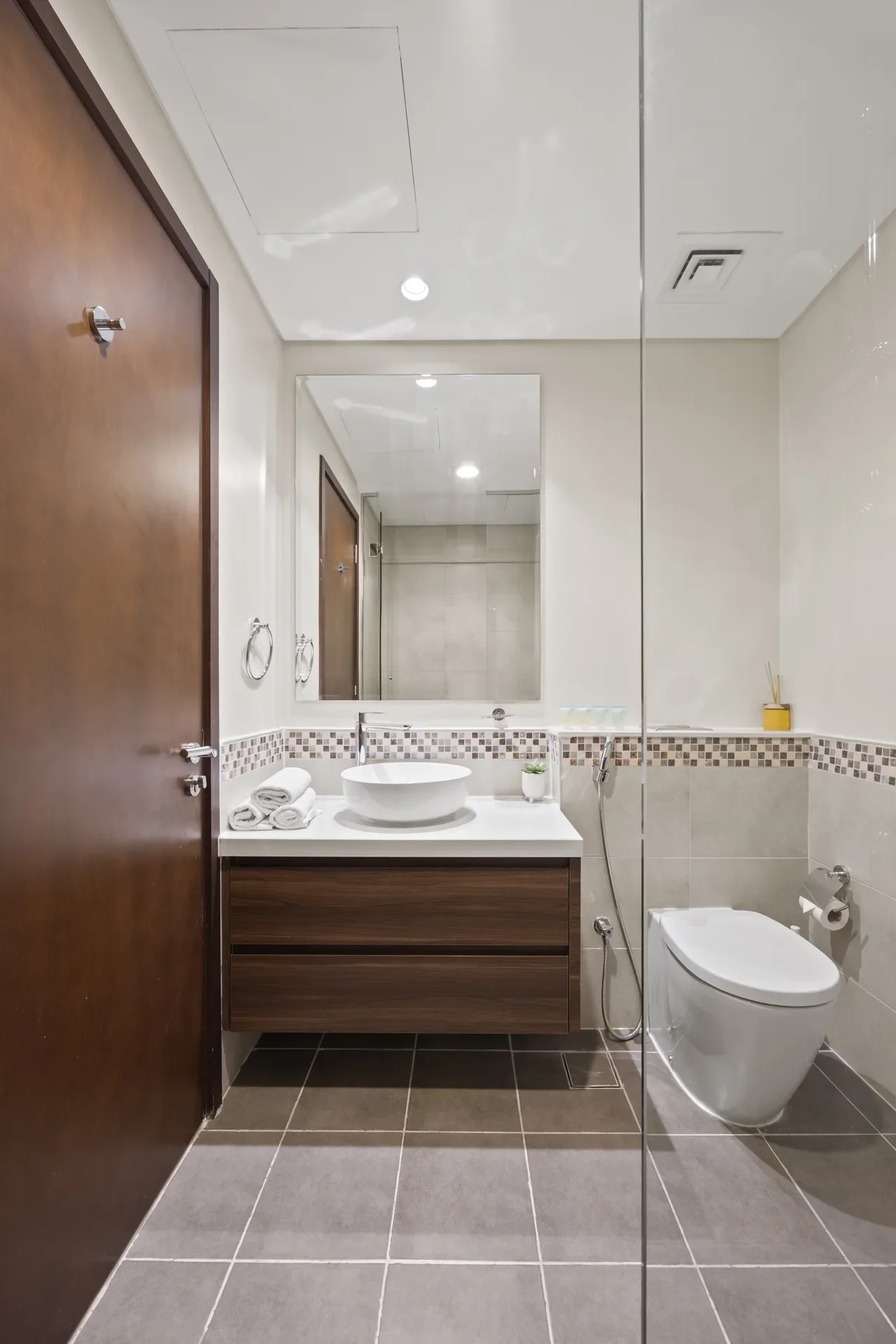 Modern bathroom with wood vanity, white vessel sink, large mirror, and glass shower beside a wooden door.