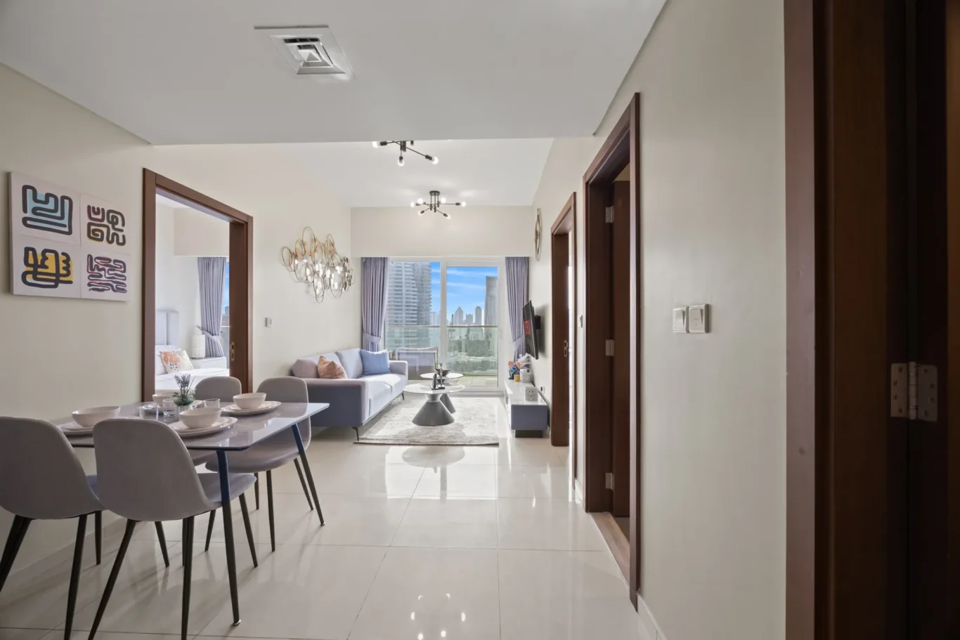 Bright open-plan living and dining area with a gray sofa, dining table, and a city skyline view through large windows.