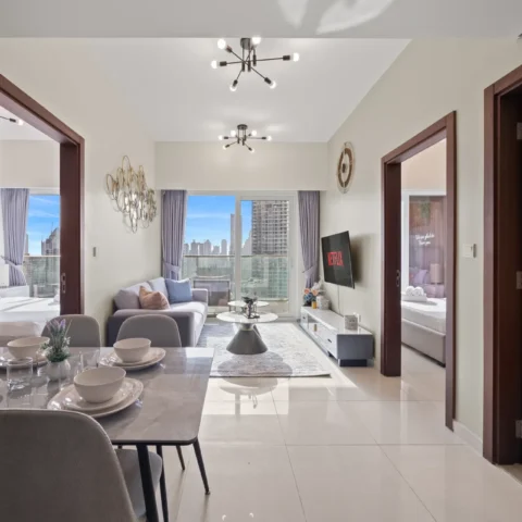 Dining area with a marble table set for six, gray chairs, and a small plant centerpiece; open living room beyond with a sofa and coffee table, city skyline visible through large windows.
