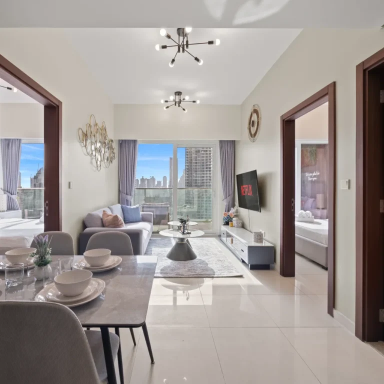 Dining area with a marble table set for six, gray chairs, and a small plant centerpiece; open living room beyond with a sofa and coffee table, city skyline visible through large windows.