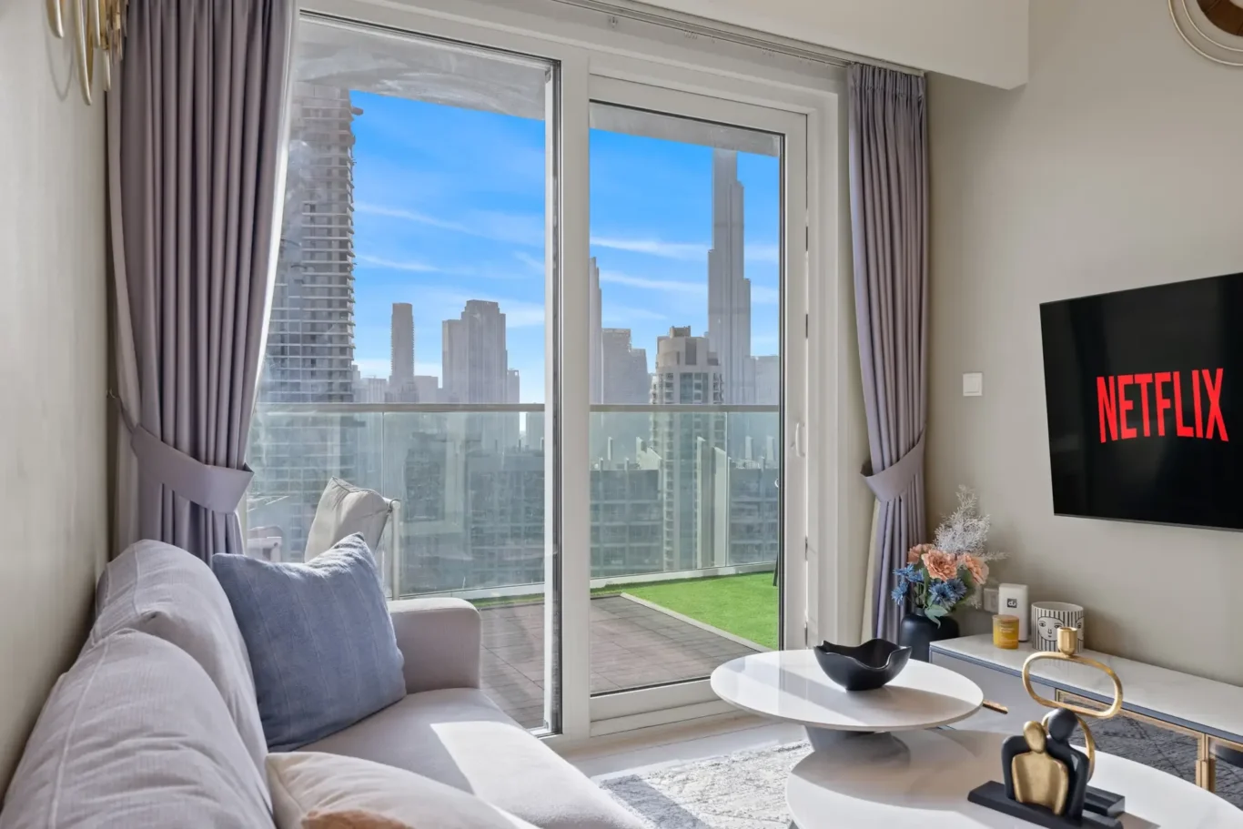 Living room with glass sliding doors to a balcony, city skyline outside, and a TV on the wall showing Netflix.
