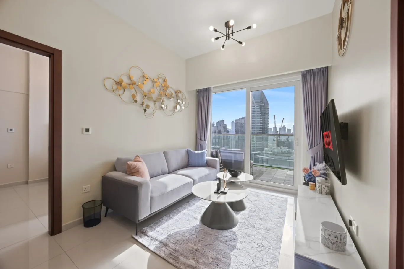 Modern living room with light gray sofa, decorative wall art, and a view of city skyscrapers through large glass doors.