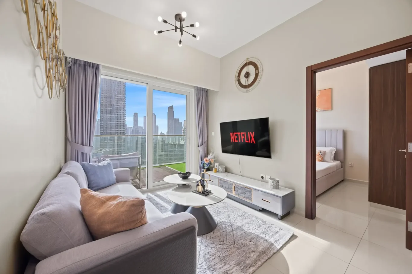 Modern living room with a Netflix screen mounted on the wall, grey sofa, and large windows with city skyline views.
