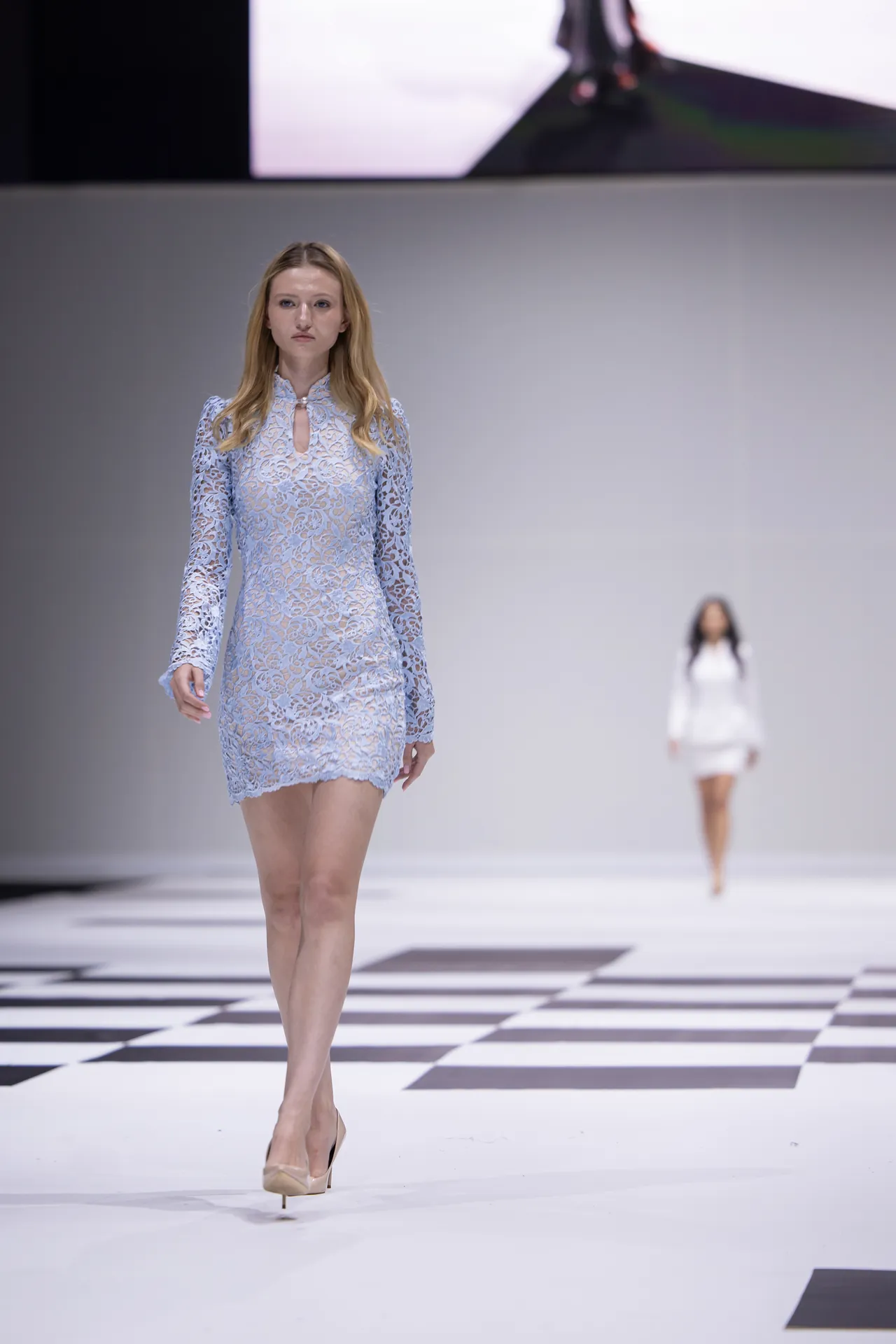 Female model walks the runway in a pale blue lace long-sleeve mini dress with a keyhole neckline.