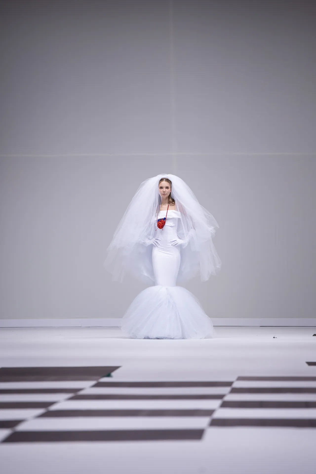 Model in a white bridal-inspired gown with a voluminous tulle veil on a minimalist runway