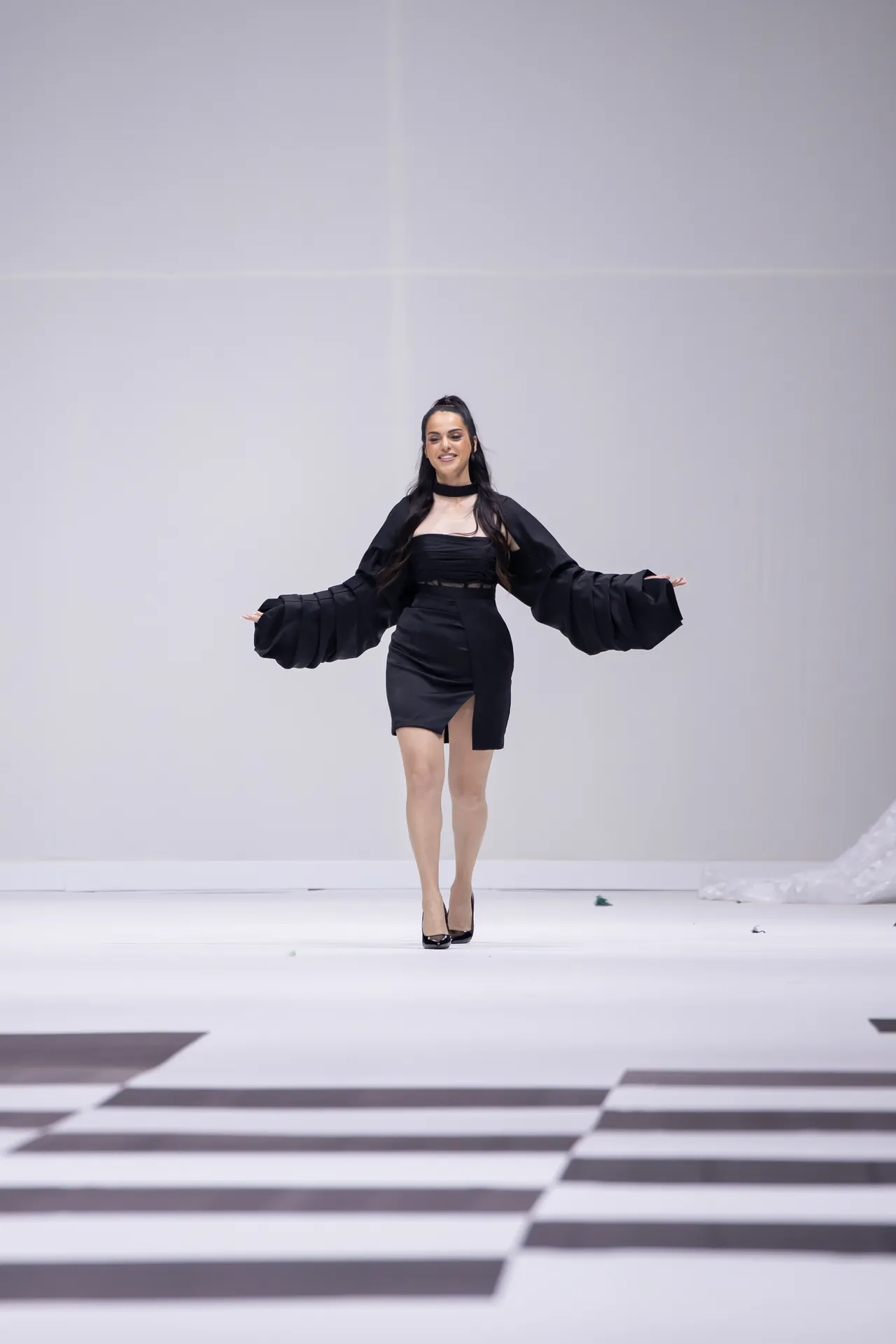 Fashion model walking a runway in a black dress with dramatic voluminous sleeves.