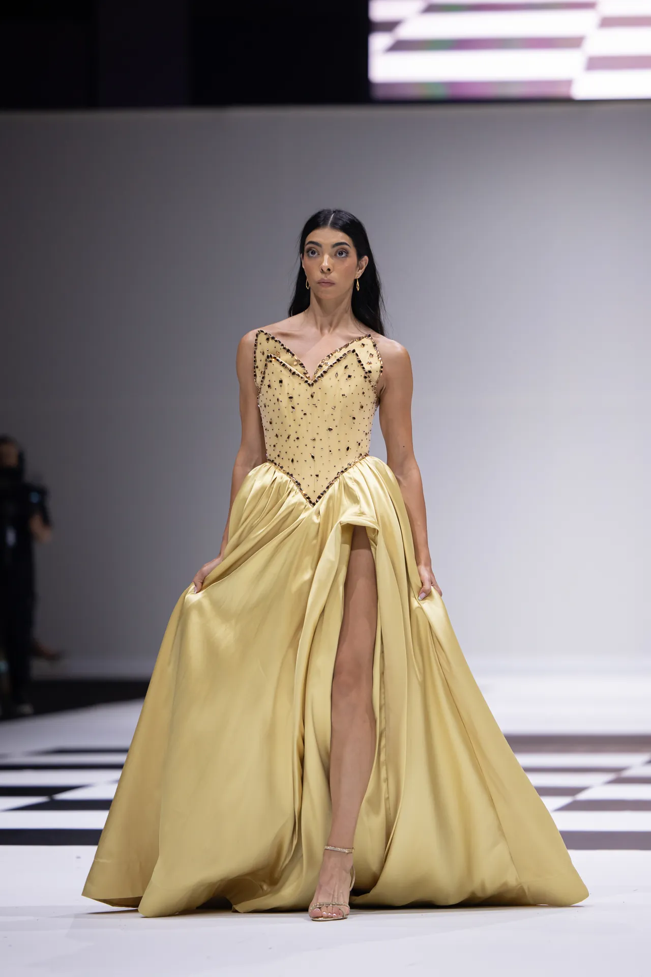 Model walks the runway in a champagne-yellow ballgown with a jeweled beaded bodice and high slit.