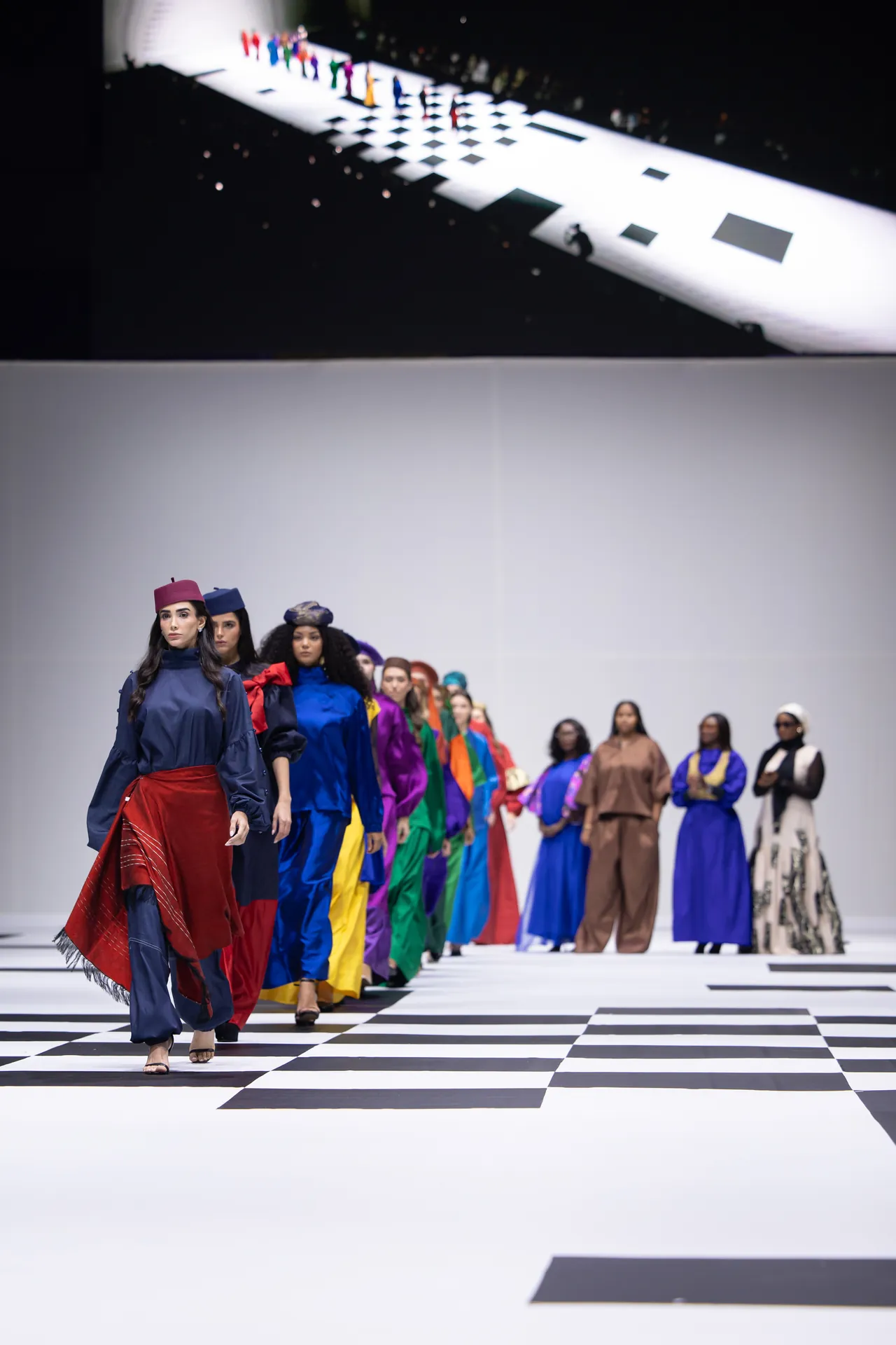 Models walk a rainbow-colored fashion show on a black-and-white checkered runway.