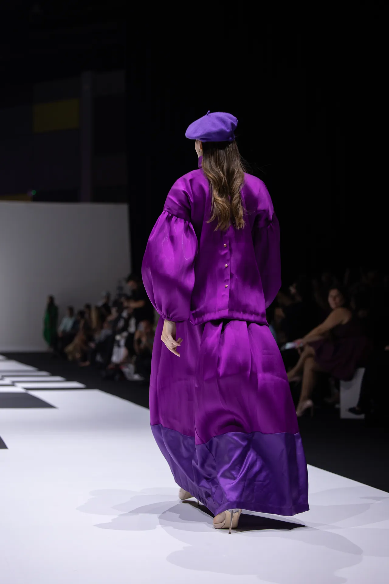 Back view of a model walking a runway in a vibrant purple outfit with a matching beret.