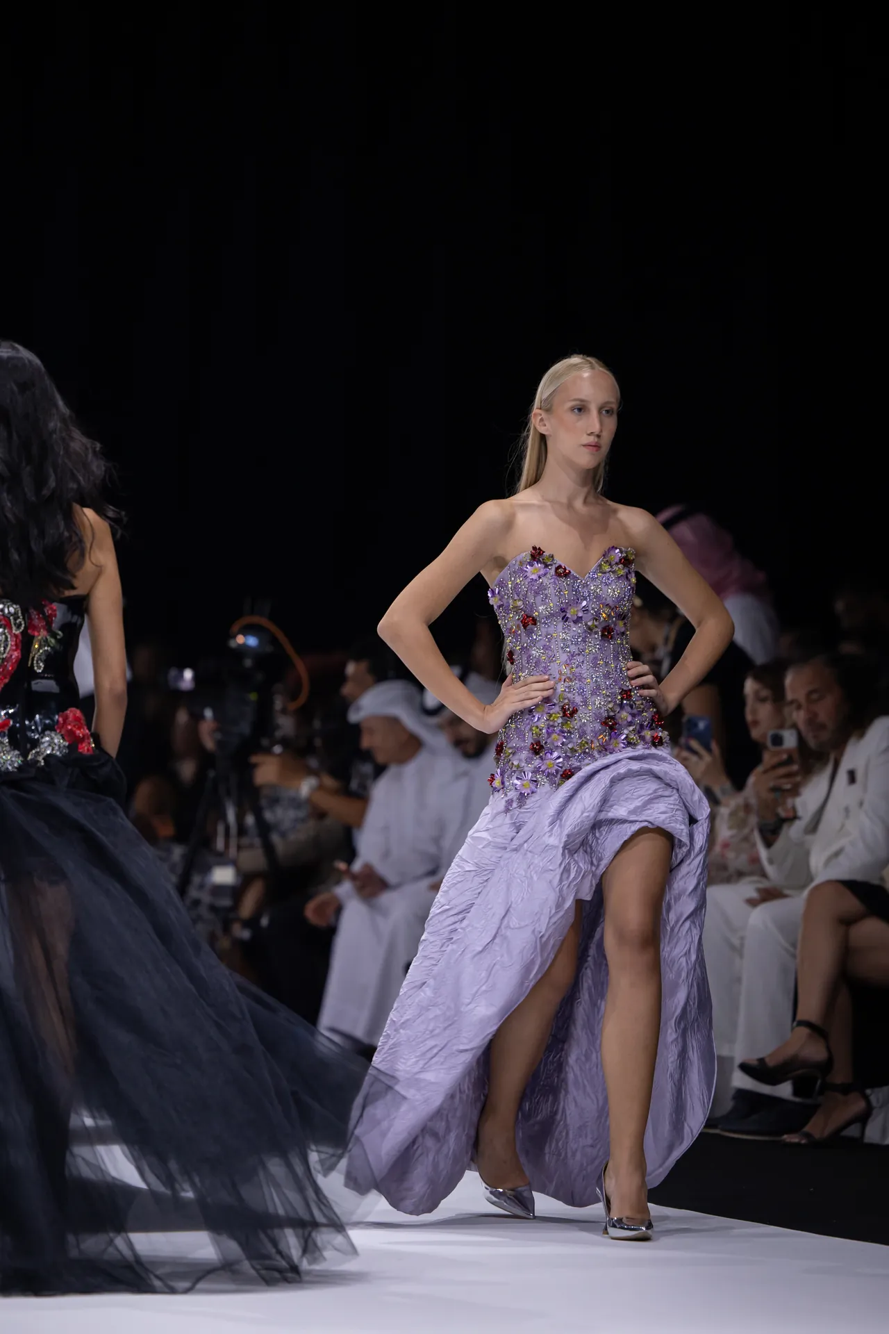 Model walks the runway in a lavender strapless gown covered in colorful floral appliqués, with a flowing train and silver heels.