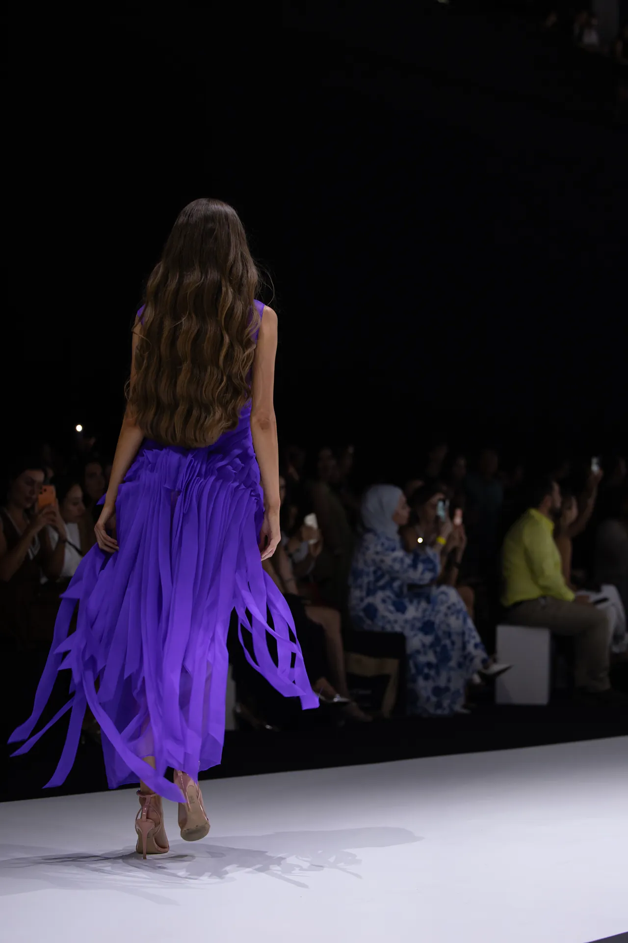 Back view of a model in a purple fringe dress walking down a runway.