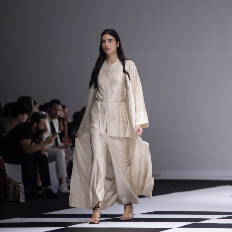 Female model walks a beige, flowing outfit down a fashion-show runway.
