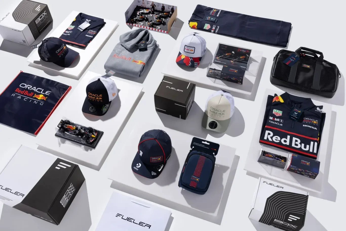 Assortment of Oracle Red Bull Racing merchandise—caps, hoodies, polo shirts, bags and boxed accessories on white display stands.