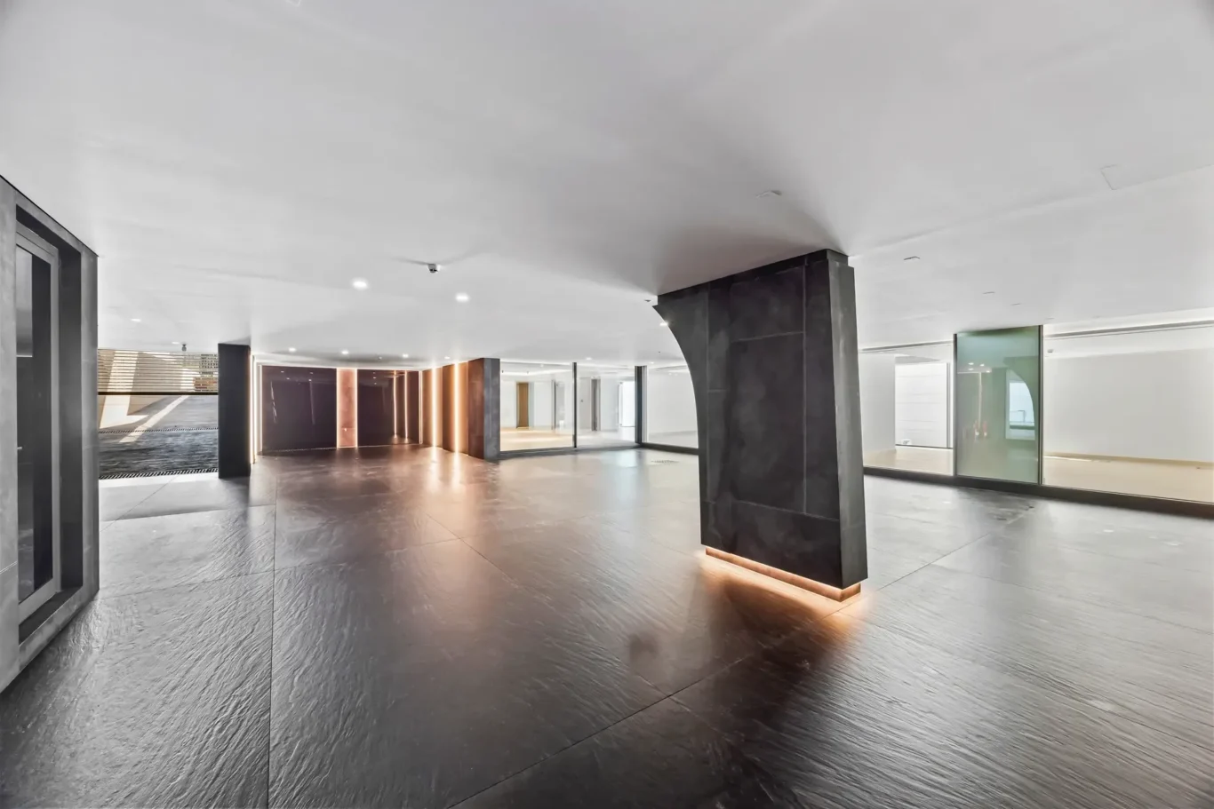 Interior of a modern lobby with dark stone columns, glossy floor tiles, and warm backlit wall panels on the left.
