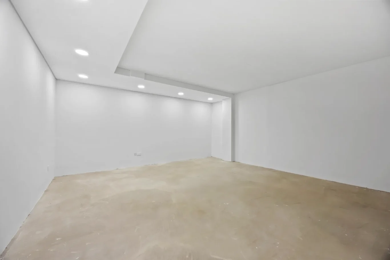 Empty white, unfinished room with recessed ceiling lights and a bare concrete floor