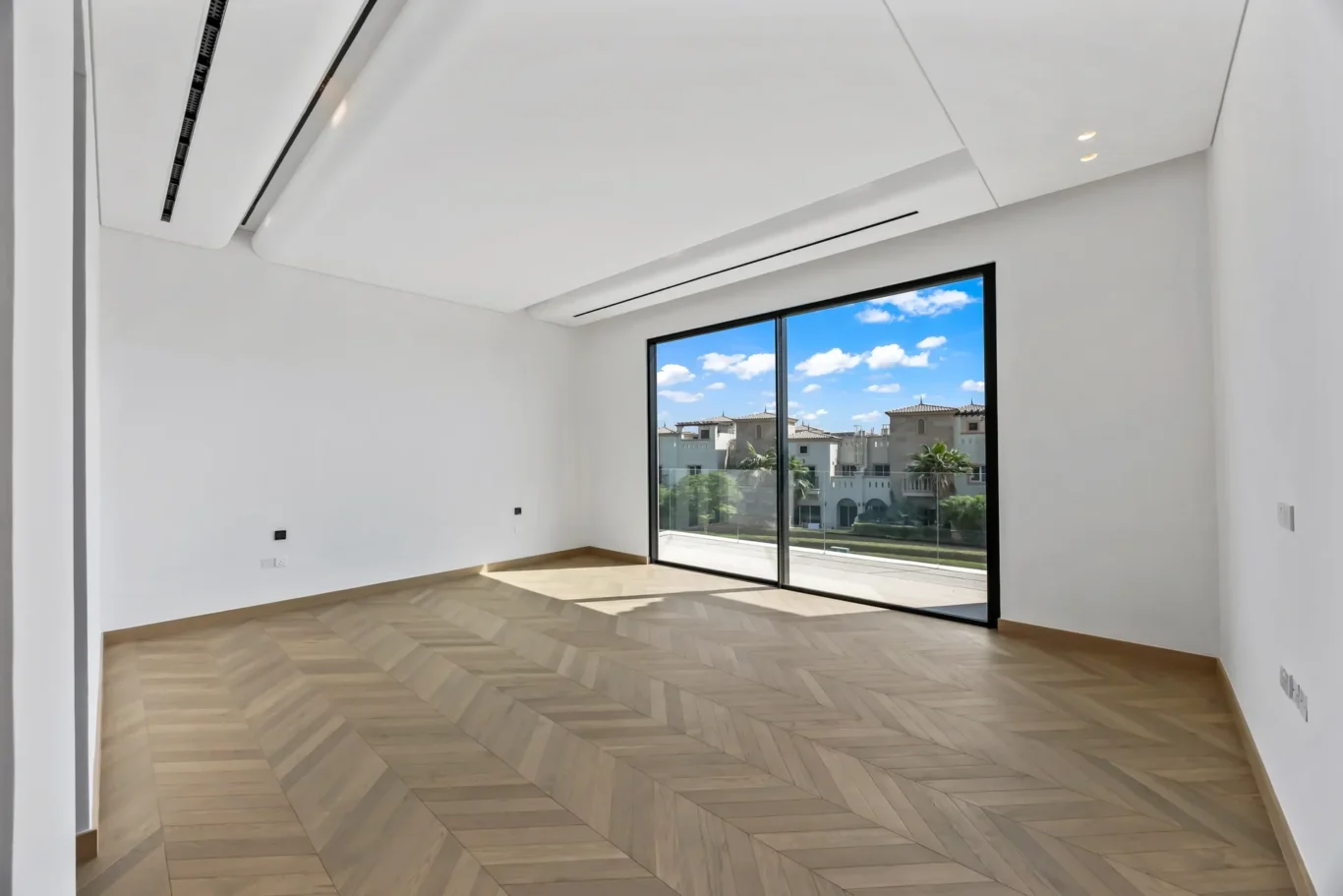 Empty white room with a large black-framed sliding glass door and a view of houses outside outside, bright and open.