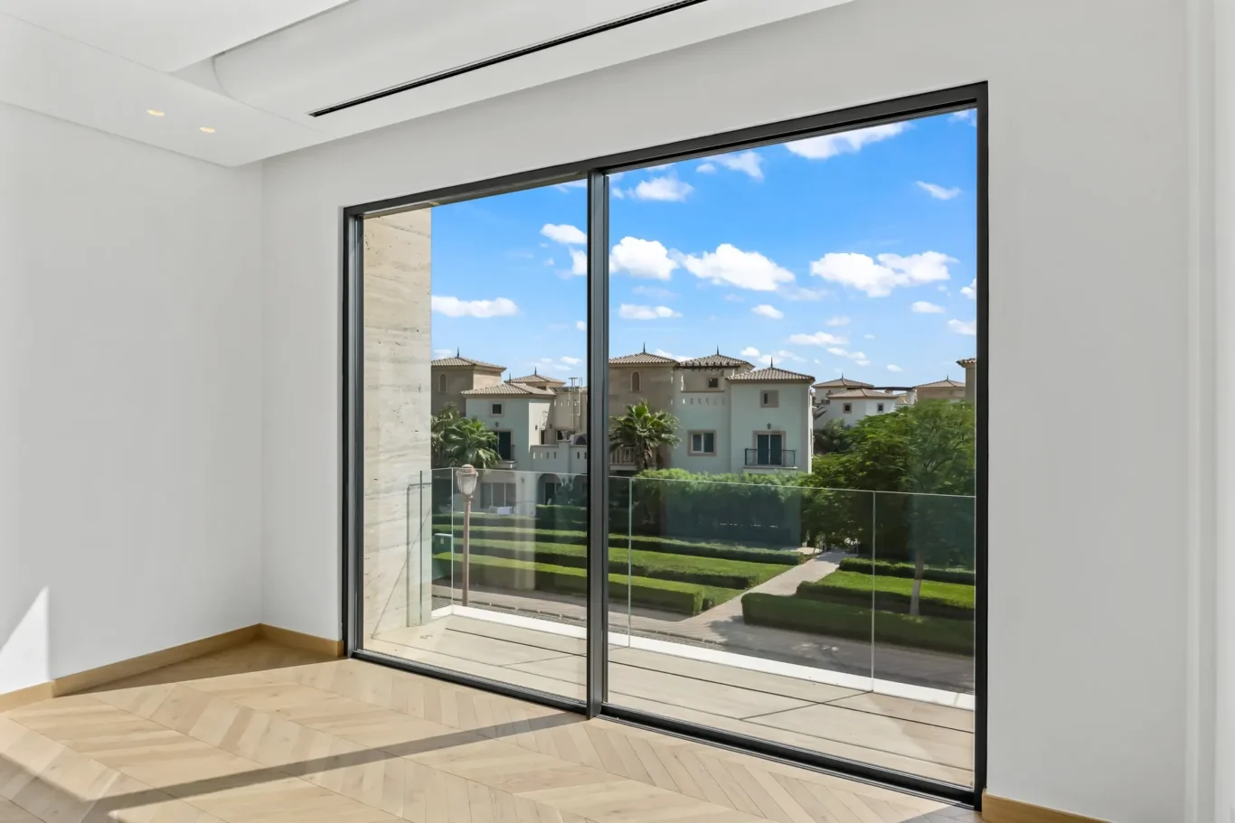 Modern interior with large black-framed sliding glass doors revealing a sunny residential complex outside