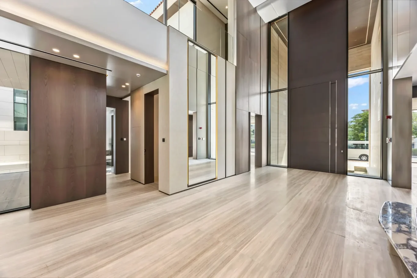 Modern office lobby with floor-to-ceiling glass, wood wall panels, and light striped flooring, bathed in natural light.