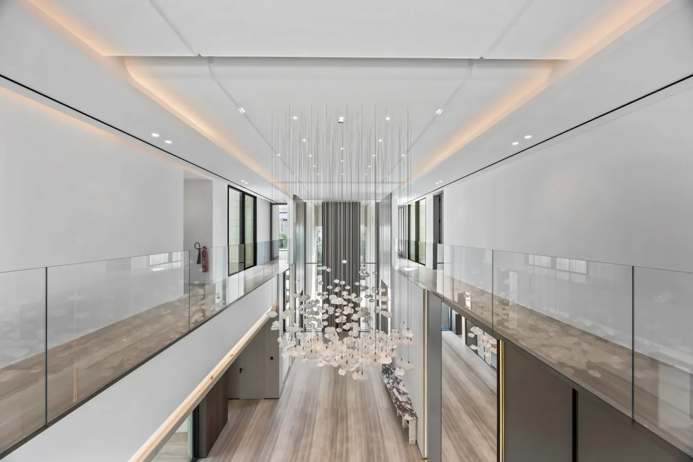 Interior atrium with glass balcony and a vertical sculpture of hanging glass orbs and rods over a marble floor.