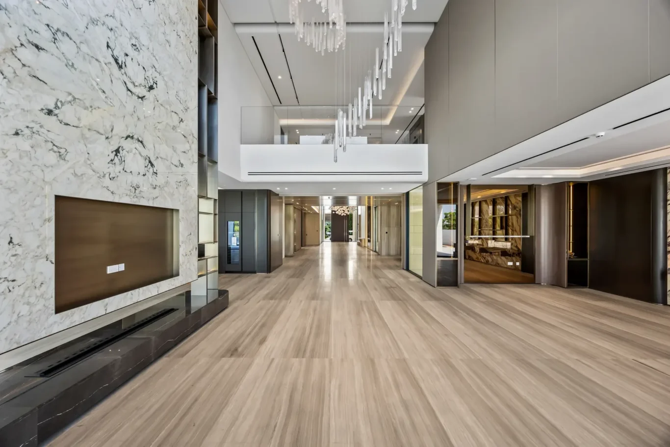 Luxurious modern lobby interior with a marble feature wall and built-in fireplace on the left, a wide hallway, and a hanging crystal chandelier.