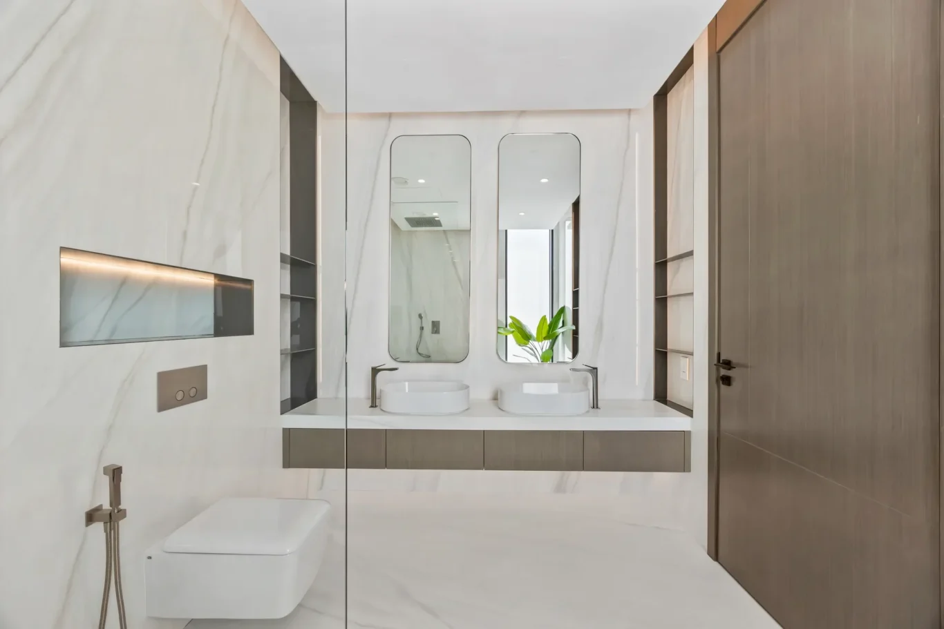 Modern white bathroom with marble walls and a double-sink vanity, two oval mirrors, and a glass shower enclosure.