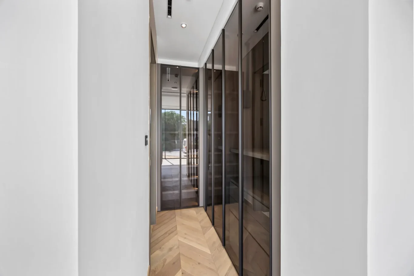 Narrow corridor with glass-fronted elevators lining one wall and chevron wood floor.