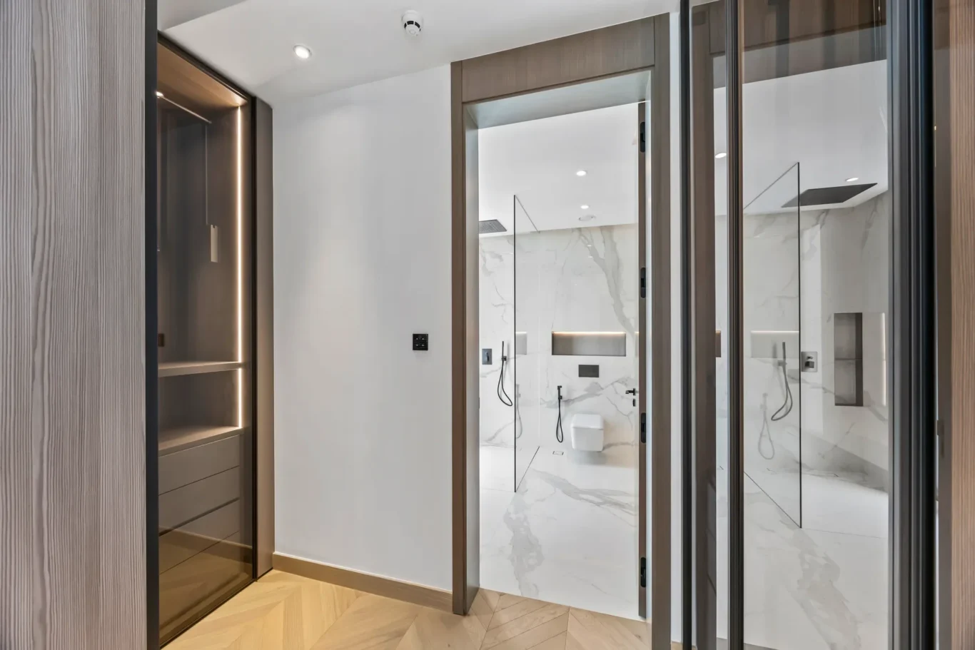 Contemporary bathroom seen through wooden-framed glass doors, featuring marble walls, a glass shower enclosure, and built-in niches.