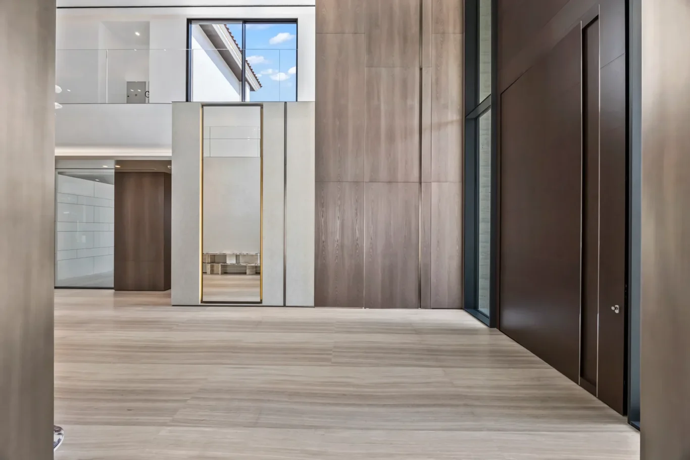 Modern showroom hallway with wood-paneled walls, light flooring, and tall brown doors on the right.