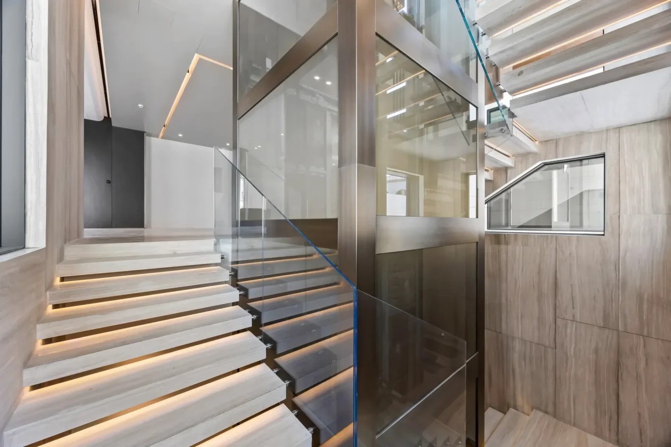 Modern interior staircase with floating wooden steps, glass railing, and metal framework in a bright lobby area.