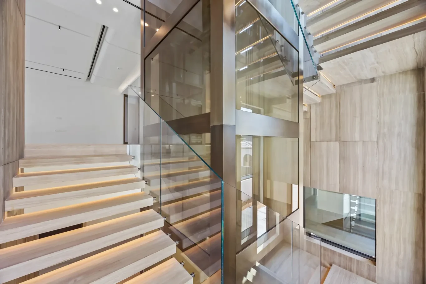 Modern interior stairwell with glass railing, floating wooden steps, and marble walls reflecting light.