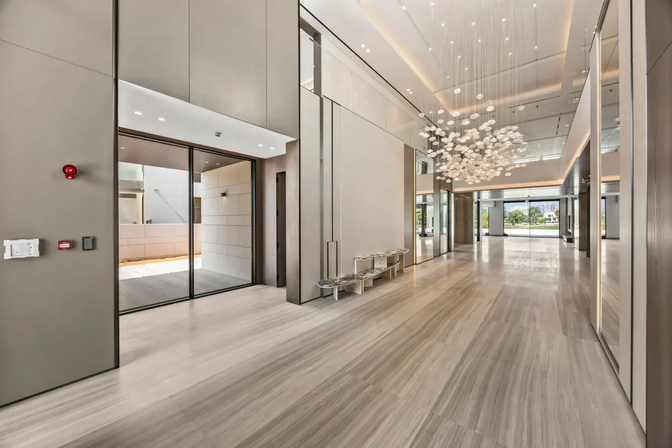 Modern lobby with grey marble walls, glass doors, and a hanging orb chandelier stretching across the ceiling.