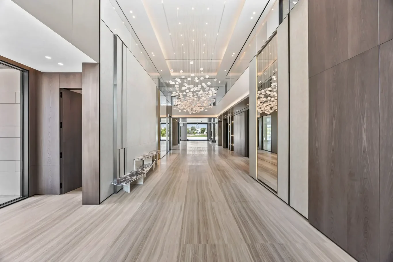Luxurious hotel lobby hallway with marble floors, glass walls, and a clustered chandelier hanging from the ceiling.