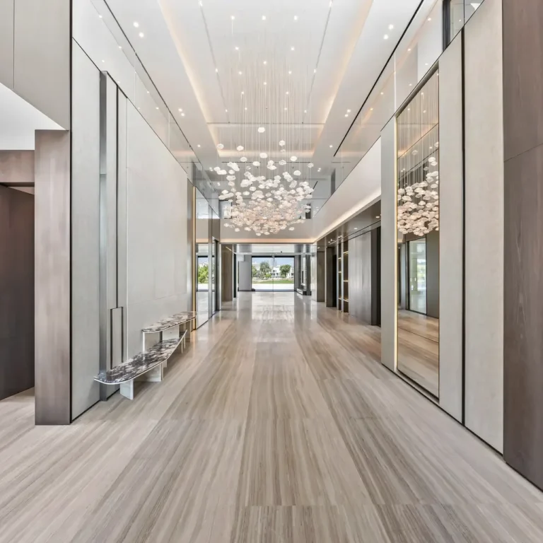 Luxurious hotel lobby hallway with marble floors, glass walls, and a clustered chandelier hanging from the ceiling.