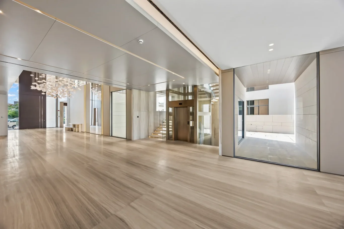 Modern hotel lobby with polished marble floors, glass walls, and an open elevator near a staircase.