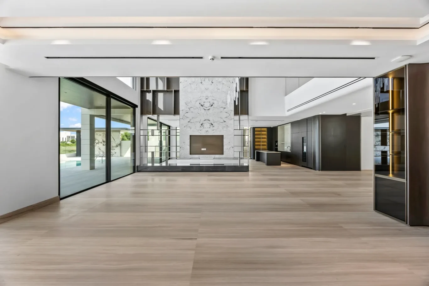 Open-concept living area with a marble accent wall featuring a built-in fireplace, glass walls, and a modern kitchen in the background.
